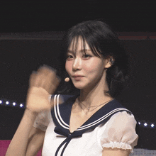a woman wearing a sailor 's uniform looks at the camera and waves her hand