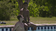 two men sit on the edge of a swimming pool