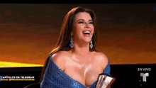 a woman in a blue dress is holding a trophy and laughing on a television show .