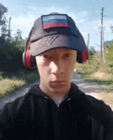 a young man wearing a baseball cap and headphones is standing on a dirt road .