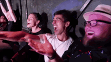 a group of people are sitting in a dark room with their arms outstretched and laughing