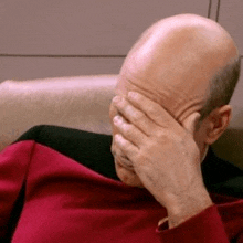 a man in a red shirt is covering his face with his hand .