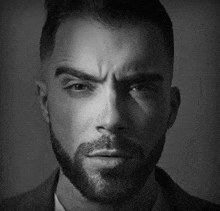 a black and white photo of a man with a beard wearing a suit .