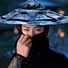 a man wearing a hat and a mask is covering his face with his hand .