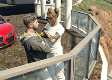 a man and a woman standing on a balcony with a red car behind them