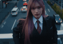 a girl with pink hair wearing a suit and tie looks at the camera