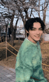 a young man wearing a green sweater and a necklace smiles for the camera