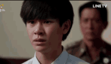 a man in a white shirt stands in front of a man in a military uniform with line tv written on the bottom of the screen