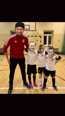a man in a red adidas jacket poses with three young boys with their faces painted