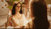 a woman wearing glasses is talking to another woman while holding a purse .