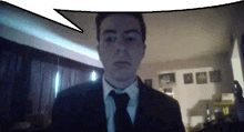 a man in a suit and tie looks at the camera with a speech bubble above him