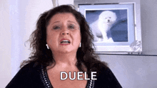 a woman is crying in front of a picture of a dog and the word duele is on her face .