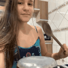 a woman in a blue tank top is holding a wooden spoon