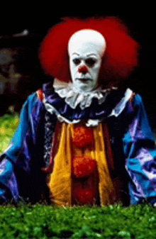 a clown is sitting in the grass wearing a blue and yellow outfit .