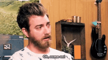 a man with a beard is standing in front of a guitar in a room .