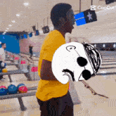 a man in a yellow shirt is holding a bowling ball with a drawing of a man on it