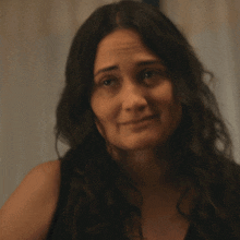 a woman with long dark hair and a black tank top is smiling