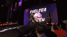 two women are dancing in front of a large screen that says chelsea on it