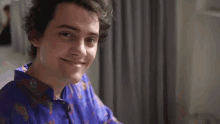 a young man wearing a purple shirt is smiling for the camera