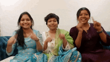 three women are sitting on a couch with their hands up