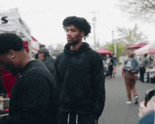 a man in a black hoodie stands in a crowd