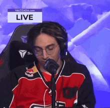 a man in a red and black jersey is sitting in front of a microphone .