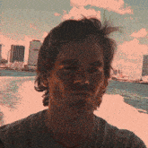 a man in a gray shirt is looking at the camera with a city in the background