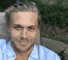 a man with blonde hair and a beard is sitting in a chair and smiling at the camera .