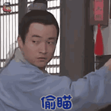 a man in a blue shirt is standing in front of a window with a red lantern .