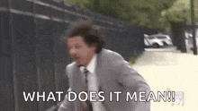 a man in a suit and tie is running down a street and saying what does it mean .