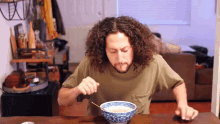 a man with curly hair is sitting at a table eating a bowl of soup
