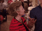 an older woman in a red and black striped shirt is talking to a man in a blue shirt .