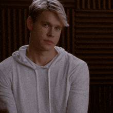 a young man wearing a white hoodie looks to the side