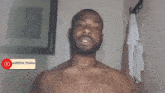 a shirtless man with a beard is standing in front of a wall with a towel hanging from it