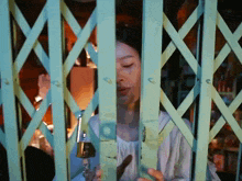 a woman is behind a green fence with a bottle in her hand