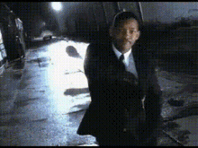 a man in a suit and tie is walking down a wet street .