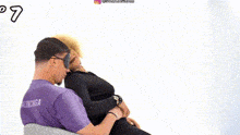 a man wearing a blindfold is sitting next to a woman in a black dress