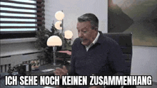 a man is sitting at a desk in an office with the words `` ich sehe noch keinen zusammenhang '' above him .