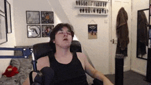 a man in a black tank top is sitting in a chair with his eyes closed in a room .