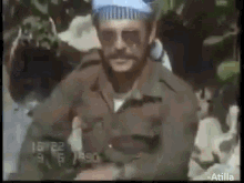 a man in a military uniform and sunglasses is standing in front of a crowd of people .