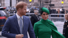 a man in a blue suit and tie and a woman in a green dress walk down the street
