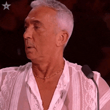 a man wearing a white shirt with a gold chain around his neck is speaking into a microphone