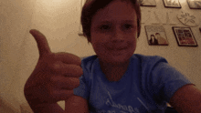 a young boy giving a thumbs up in front of a wall with pictures on it