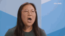 a woman wearing glasses is making a face in front of a blue wall that says elite daily on it