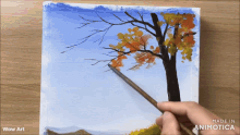 a person is painting a tree with a brush on a piece of paper that says wow art