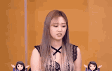 a woman with long hair is standing in front of a yellow wall with two dolls behind her .