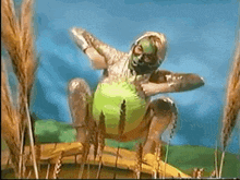 a person with a green face painted on their body is sitting in a field of wheat .