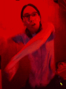 a woman wearing glasses is standing in front of a red light and making a fist .