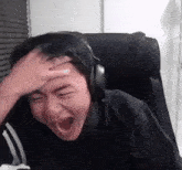 a man wearing headphones is sitting in a chair with his mouth open and holding his head .