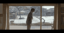 a woman is standing in front of a large window looking out to a snowy yard